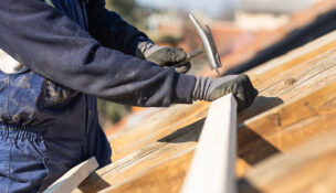 Construction roofer carpenter worker nailing wood board with hammer on roof installation work. Depositphotos