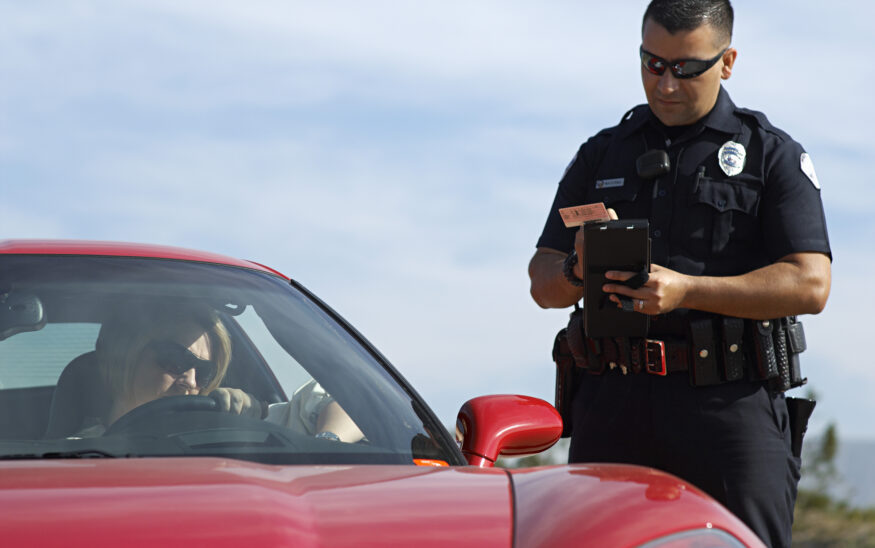 Police officer writing a ticket for woman sitting in the car